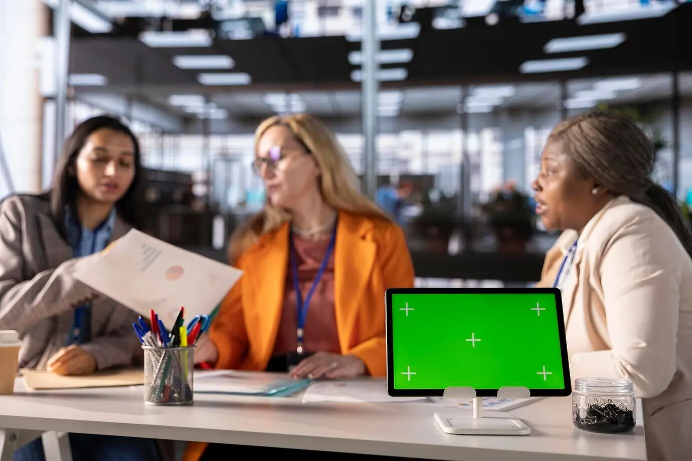 Businesswomen of diverse ethnic backgrounds working next to an isolated green screen.
